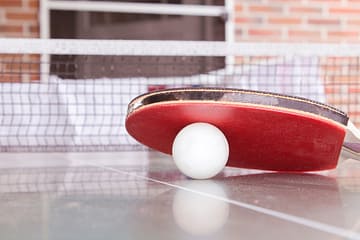 white pingpong ball beneath red table tennis paddle